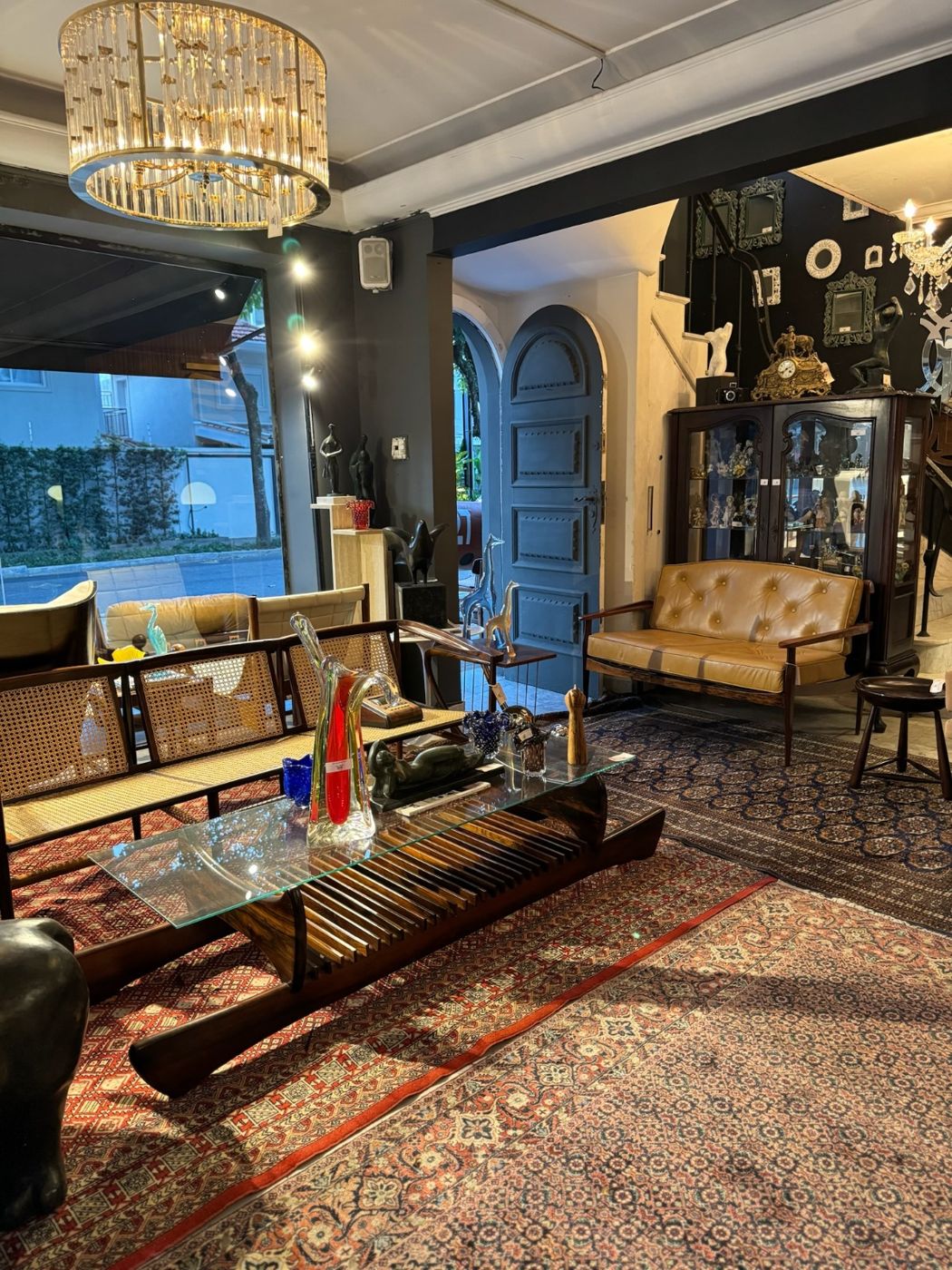 Sala com sofá de palhinha, mesa de centro em madeira e vidro, tapetes persas e lustre de cristal